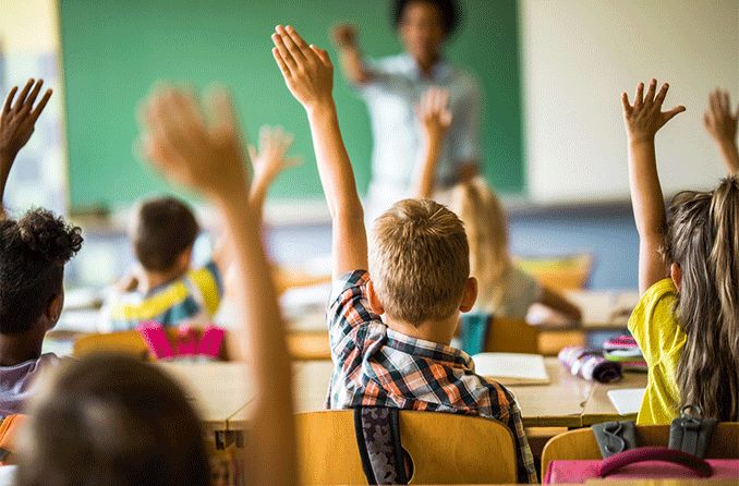 Children in classroom raising their hands with blurry background