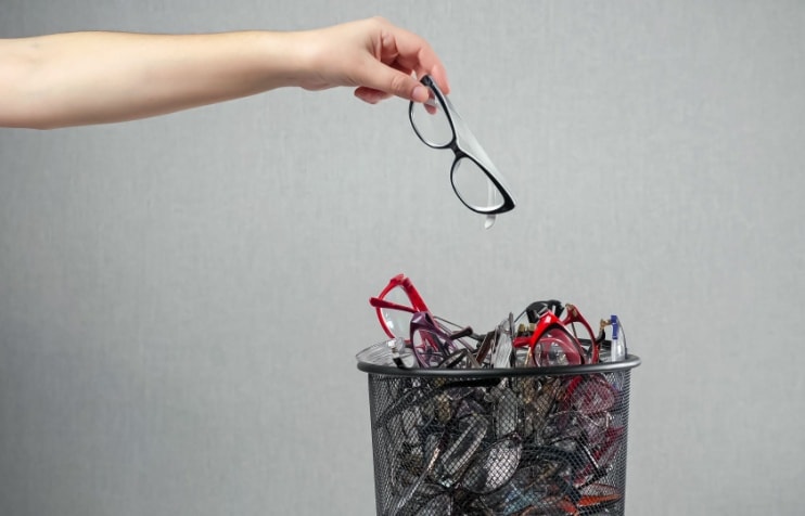 Plastic eyeglass frames being thrown into a trashcan with more glasses