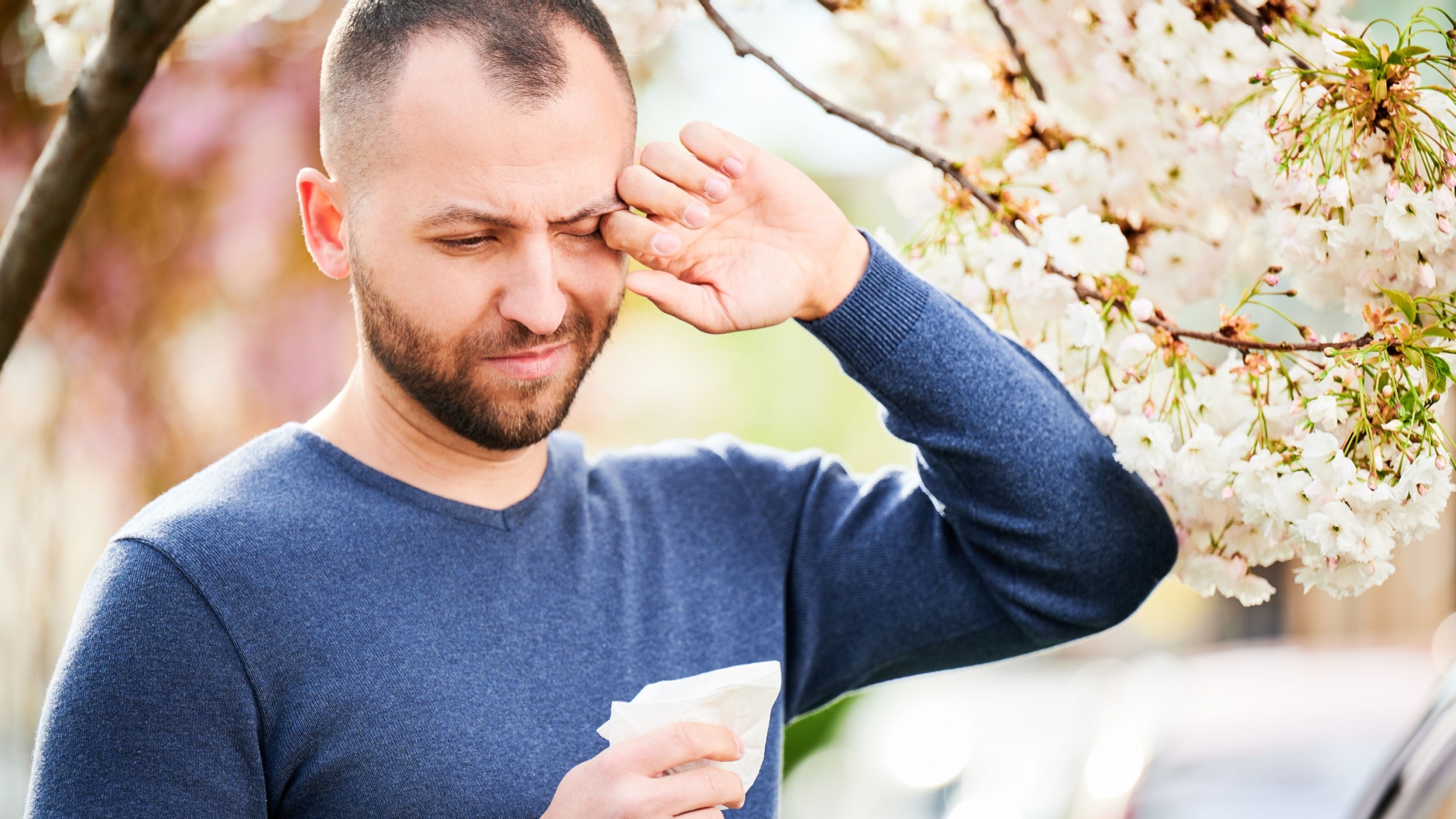 Man standing near a blooming spring tree with eye allergies Man standing near a blooming spring tree with eye allergies