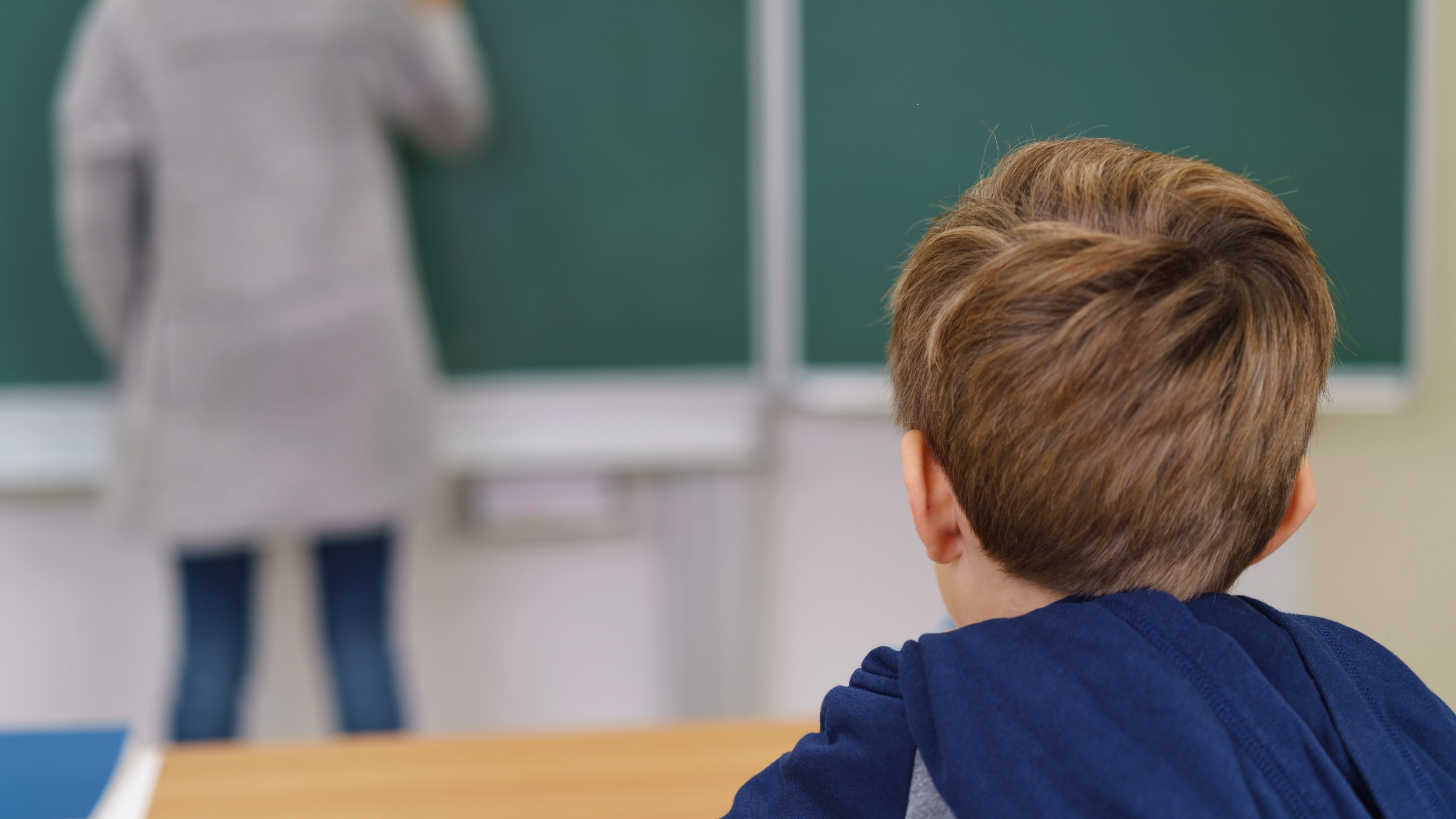 View form behind his head of a young schoolboy in class sitting at a desk View form behind his head of a young schoolboy in class sitting at a desk