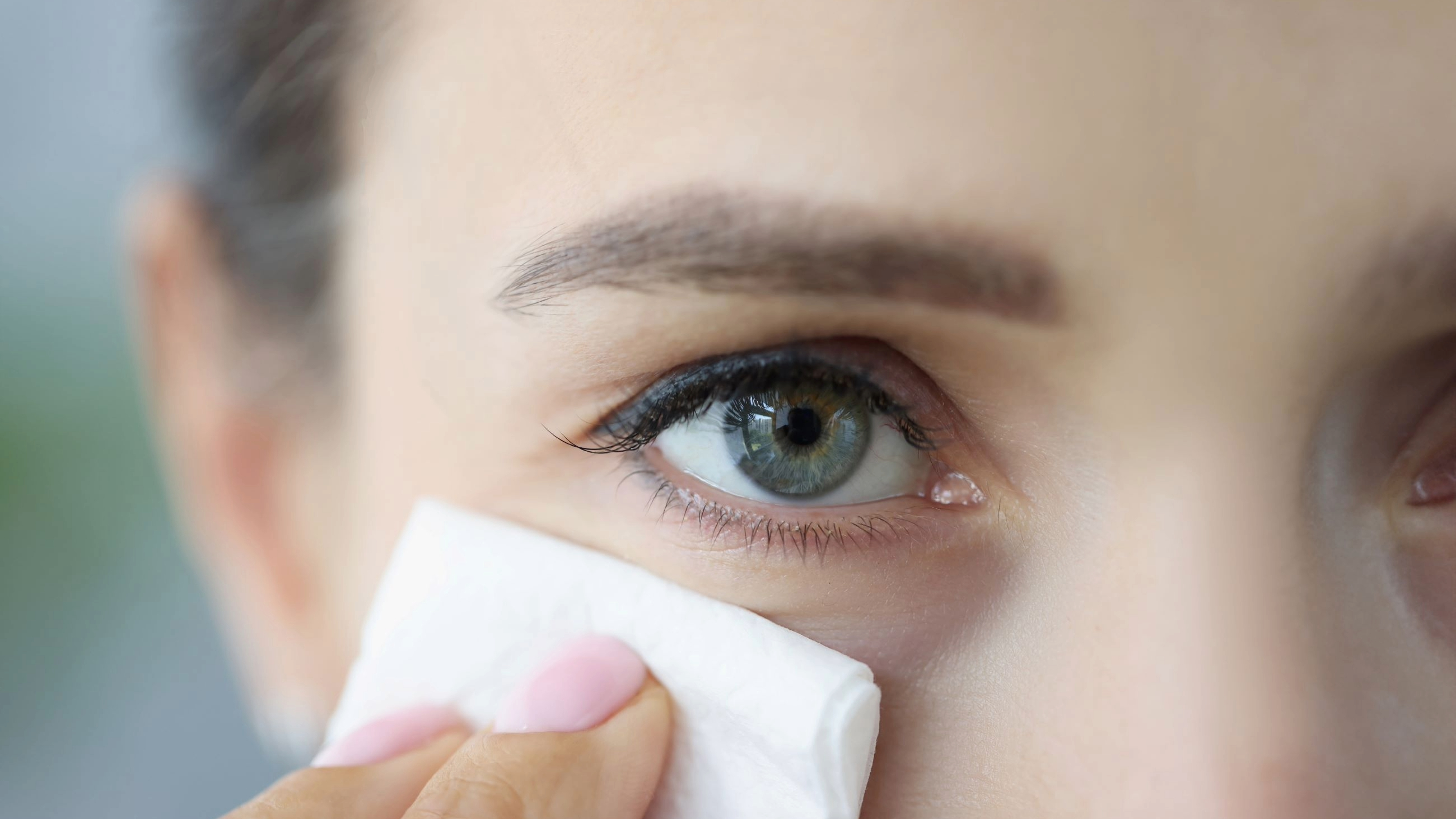 woman holding tissue up to watery eye