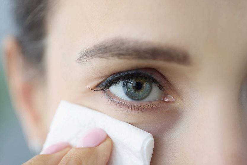 woman holding tissue up to watery eye