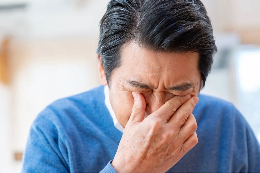 Hypopyon symptoms causing eye pain and discomfort Older man covering his eyes, experiencing eye pain and discomfort