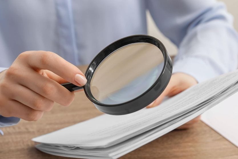woman looking at papers through a magnifying glass