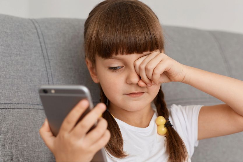 What are the effects of too much screen time? girl on mobile phone rubbing her eyes from too much screen time
