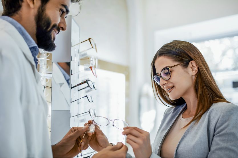 A woman with myopia wearing glasses at her optician's office wearing glasses looking at a new pair of frames.