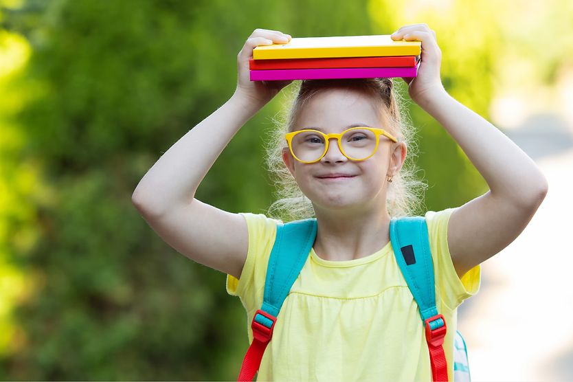 Little girl holding books and wearing a backpack