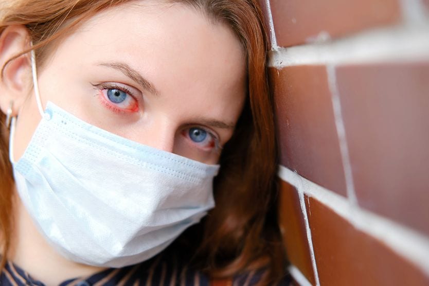 woman wearing a surgical mask who has coronavirus red eyes