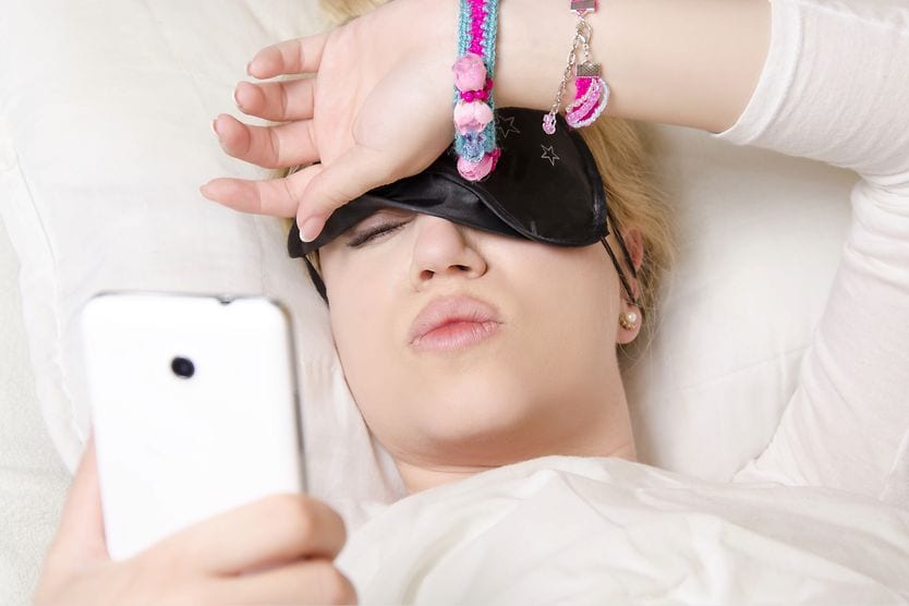woman waking up in the morning with blurry vision looking at cell phone