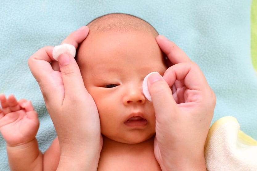 Eye discharge in newborns, babies and toddlers: Causes and treatment mother wiping away baby's eye discharge with cotton pad