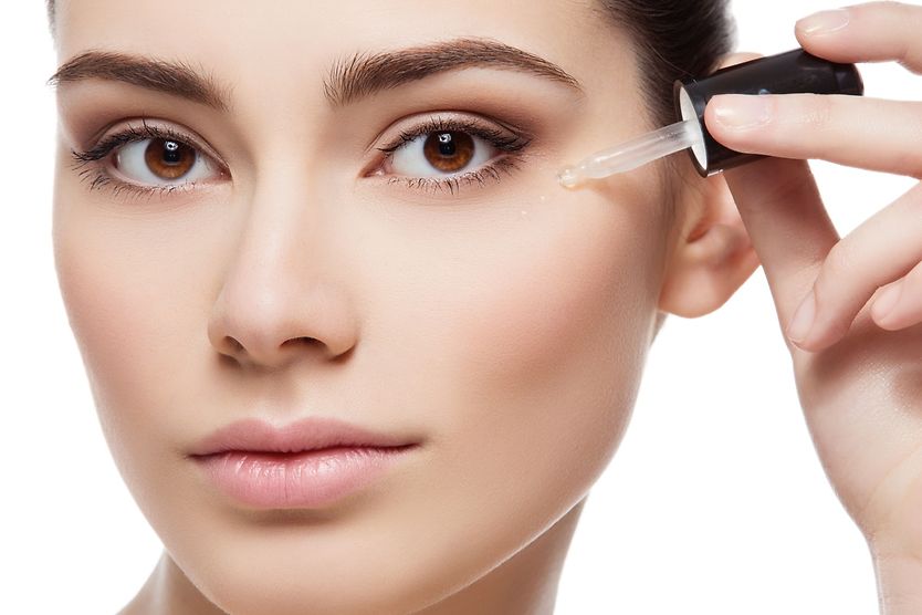 Which serum is safe to use around the eyes? Young woman applying eye serum with a serum dropper.