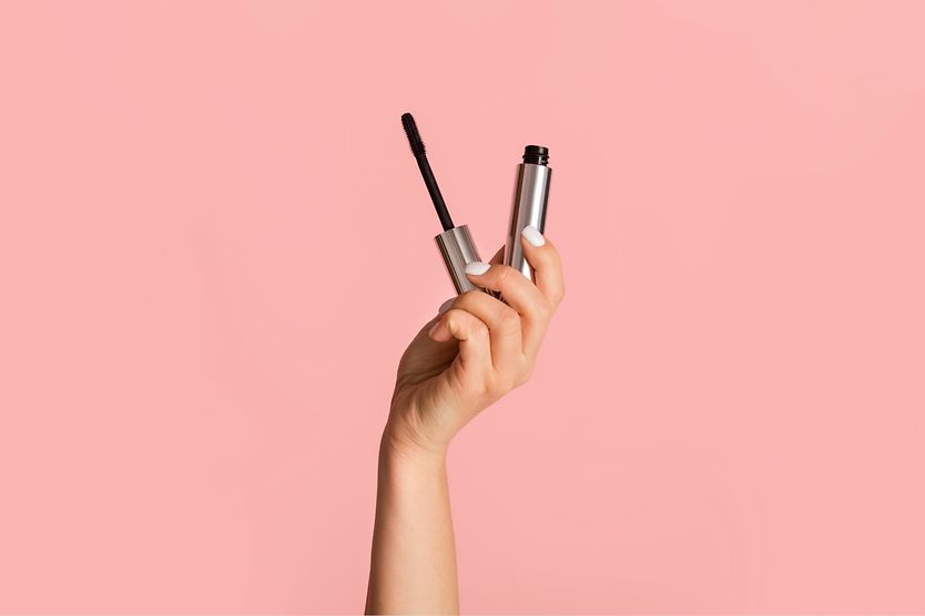 The best mascara for sensitive eyes person's hand holding hypoallergenic mascara on pink background
