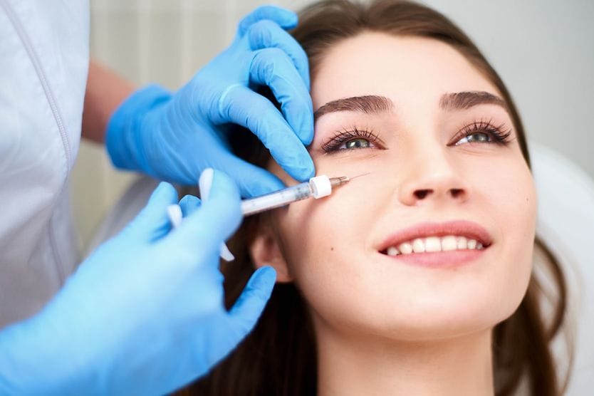 Under eye filler: Cost, safety and what to expect Woman with dark hair and brown eyes is lying back to receive under-eye filler injections.