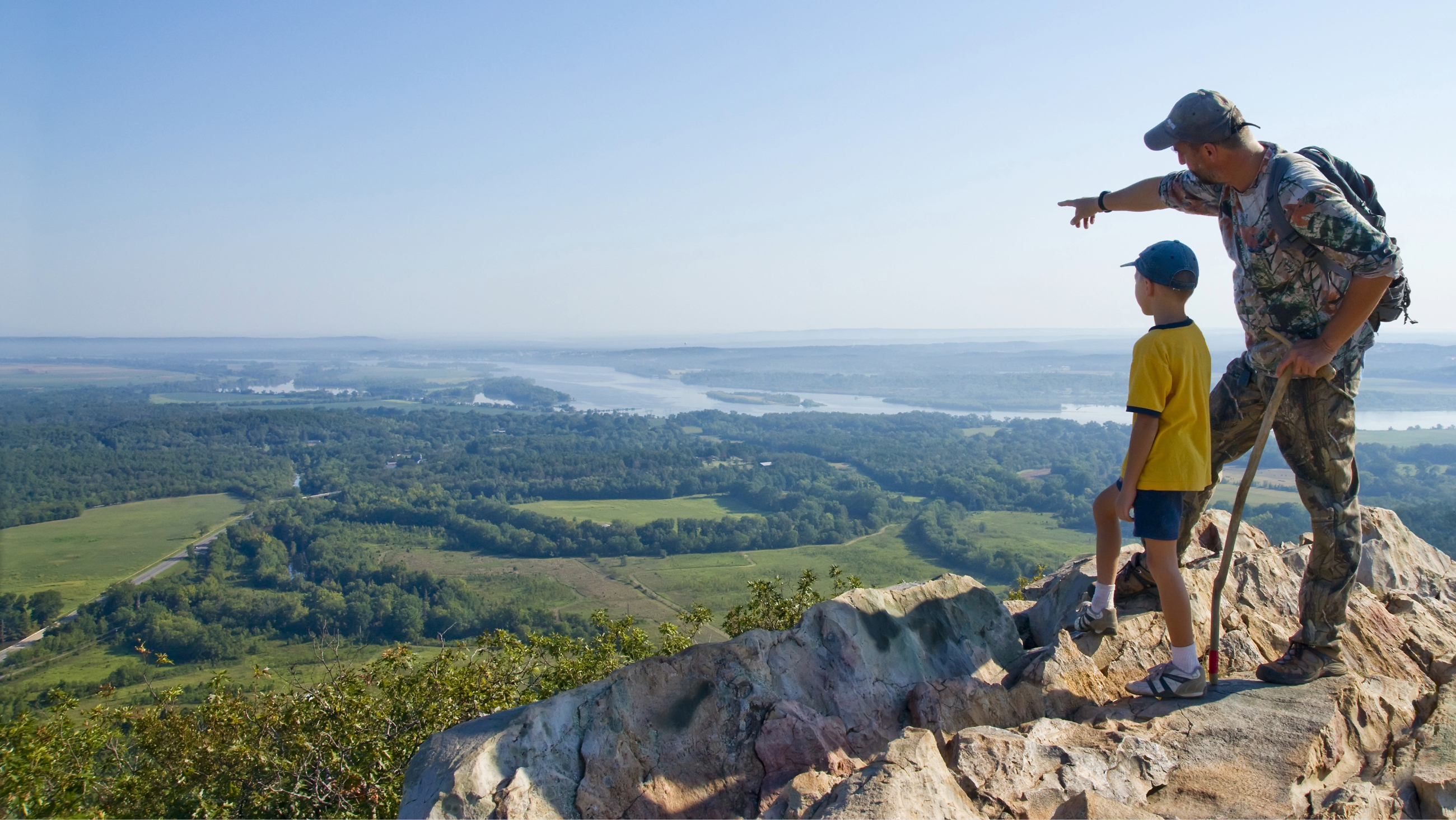 father pointing to horizon with son on top of a mountain