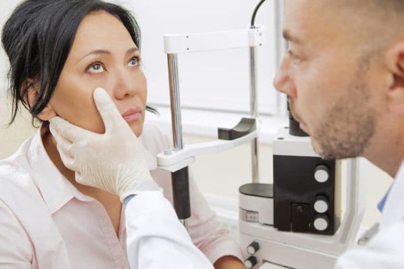 What is an optometrist? A dark-haired woman calmly looks toward the ceiling so her optometrist can examine her eyes.