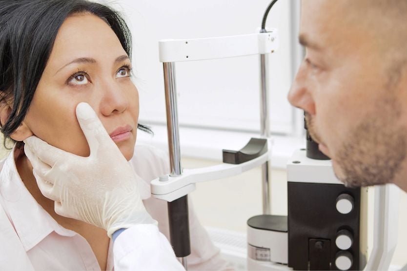 A dark-haired woman calmly looks toward the ceiling so her optometrist can examine her eyes.