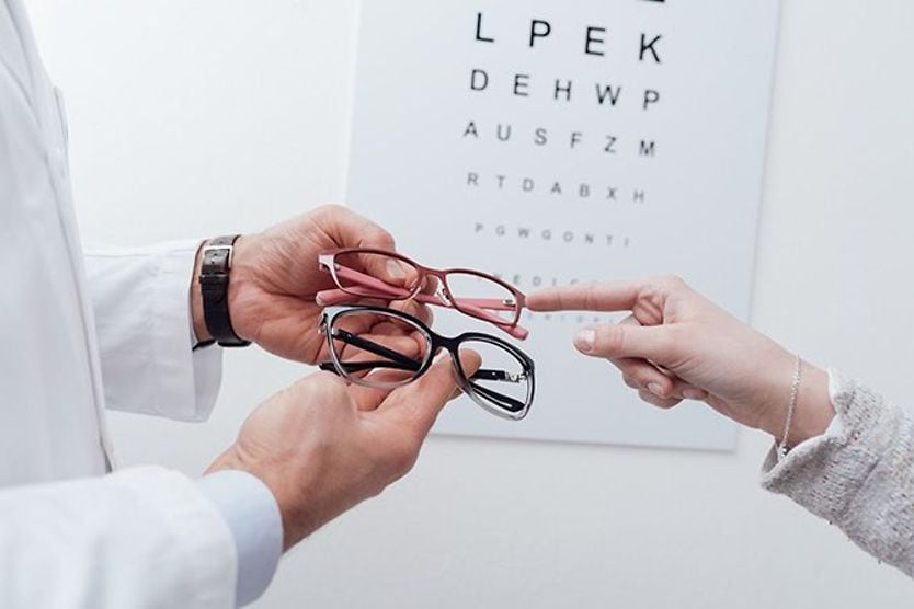 Eye chart in background with person choosing pair of eyeglasses from an optometrist