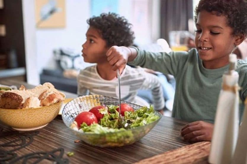 boy sitting at kitchen table serving salad