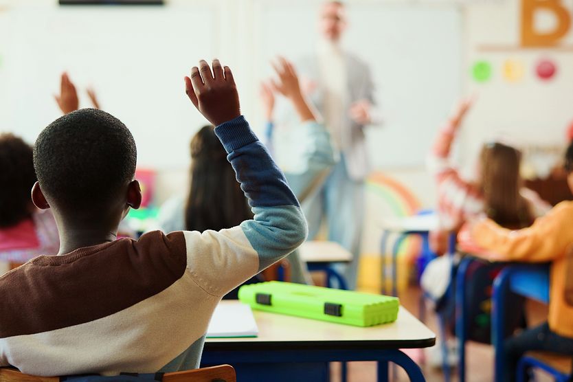 Signs That May Show Your Child Has a Vision Problem Children in classroom raising their hands with blurry background