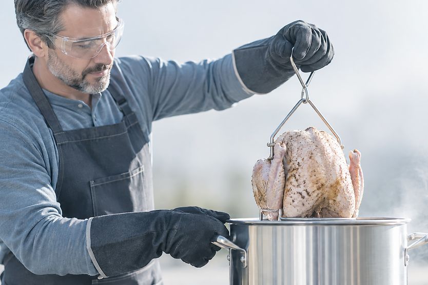 Man placing a turkey in a deep-fryer while waring safety glasses.
