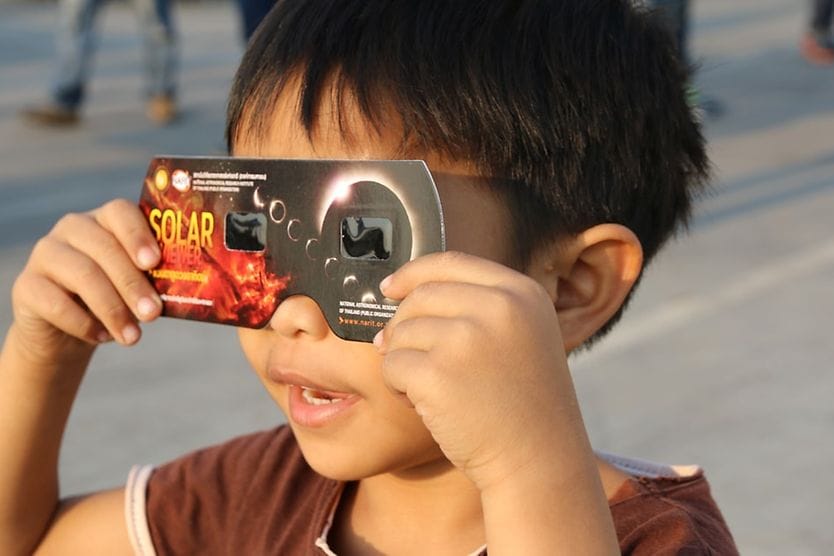 Solar eclipse eye safety: April 8 & October 2, 2024 Little boy looking through eclipse glasses looking up at the solar eclipse.