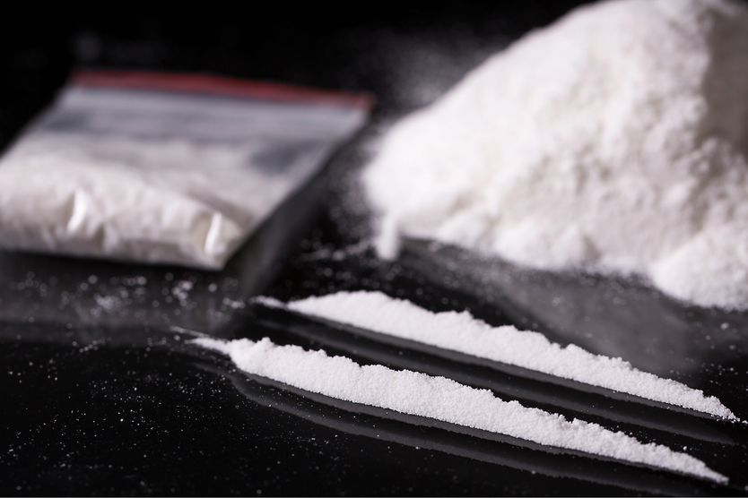Plastic packet, two lines and pile of cocaine on black background, closeup.