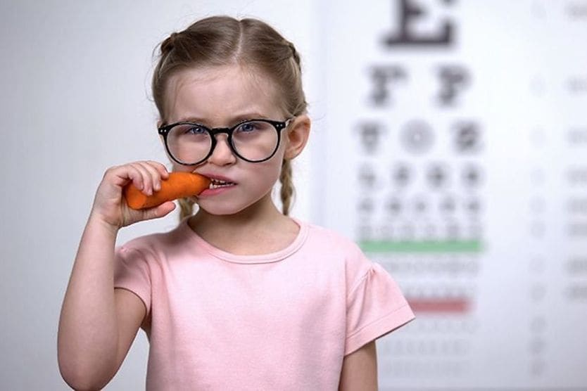 Are carrots really good for your eyes? young girl eating carrots and wearing eyeglasses
