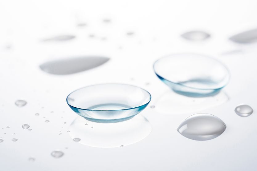 Image of two contact lenses on a glass tabletop with contact lens solution droplets.