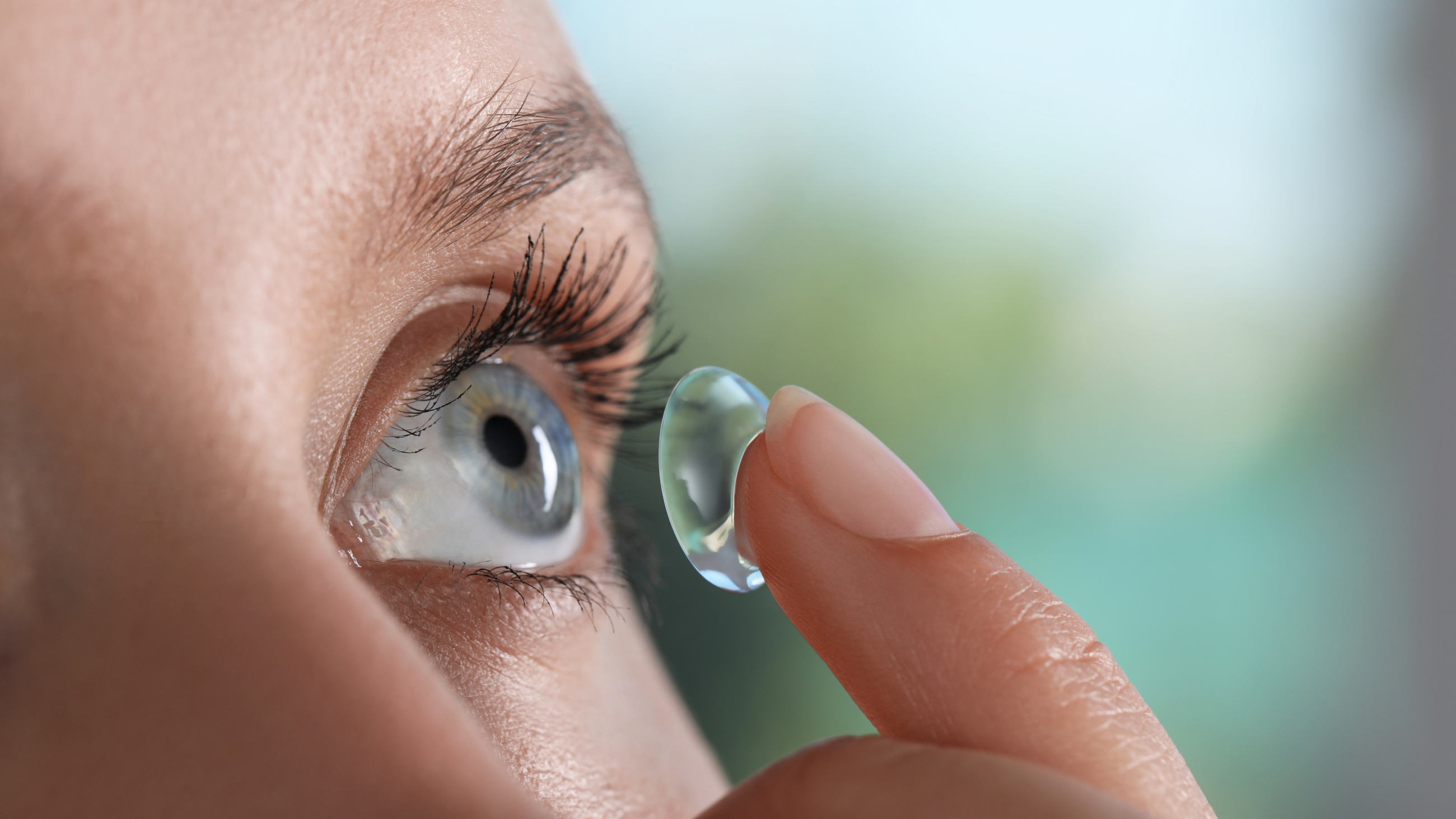 Young woman putting contact lens in her eye.