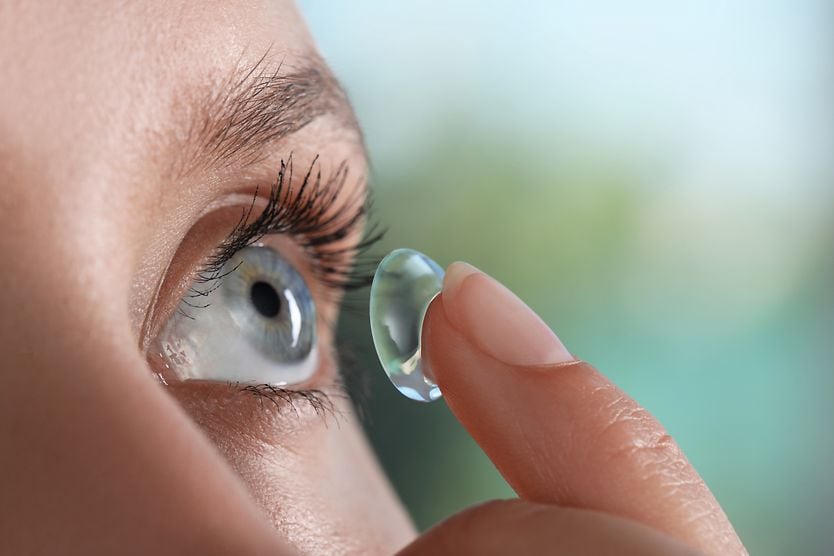 Young woman putting contact lens in her eye.