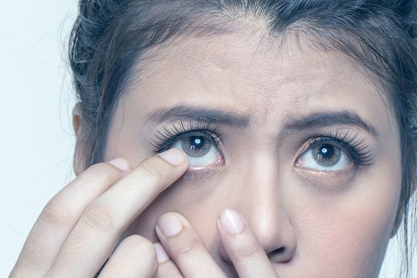 A woman with one finger near her eye as she struggles to remove a stuck contact lens. A woman with one finger near her eye as she struggles to remove a stuck contact lens.