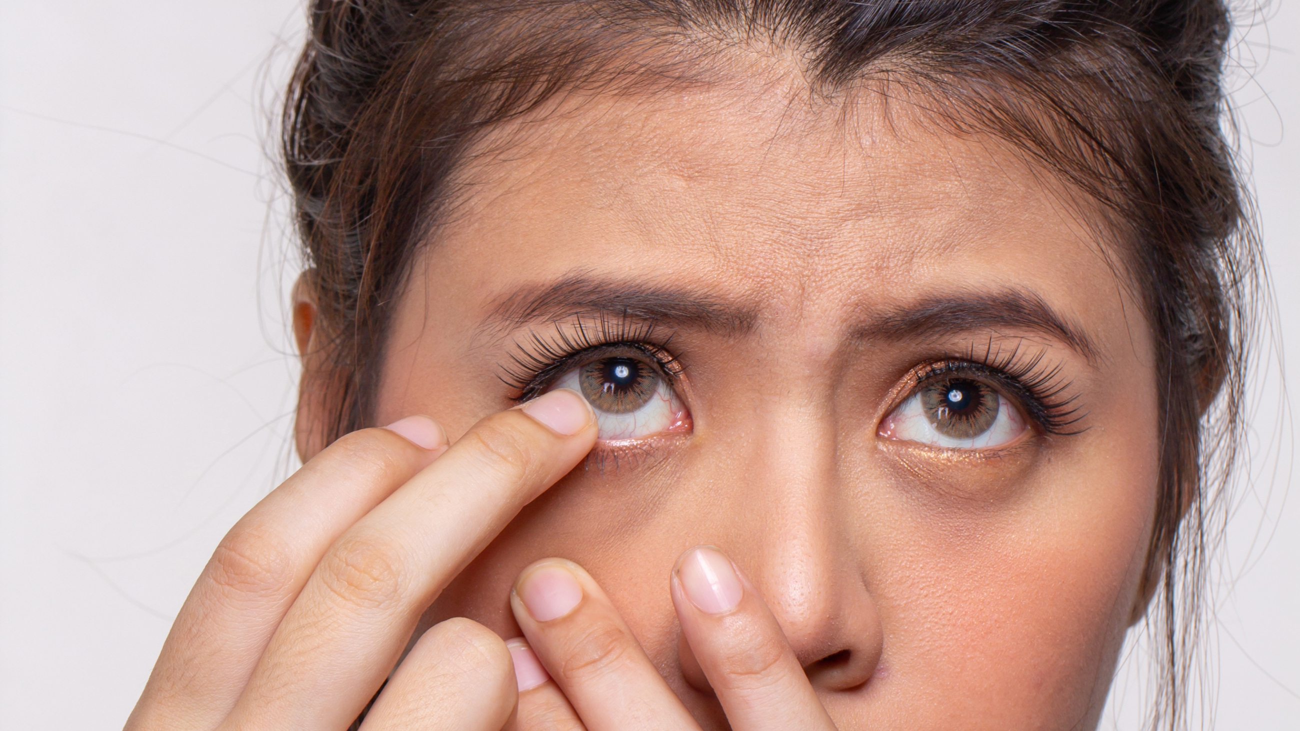 A woman with one finger near her eye as she struggles to remove a stuck contact lens.