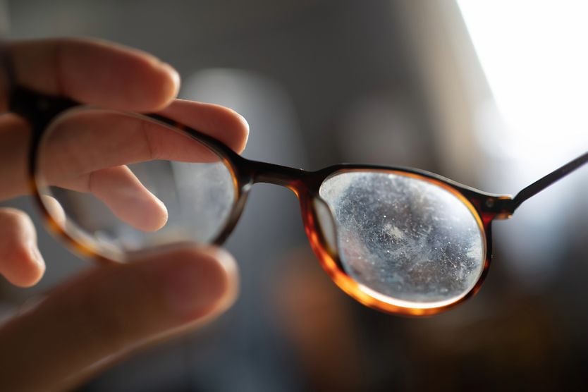 hand holding up a pair of scratched eyeglass lenses