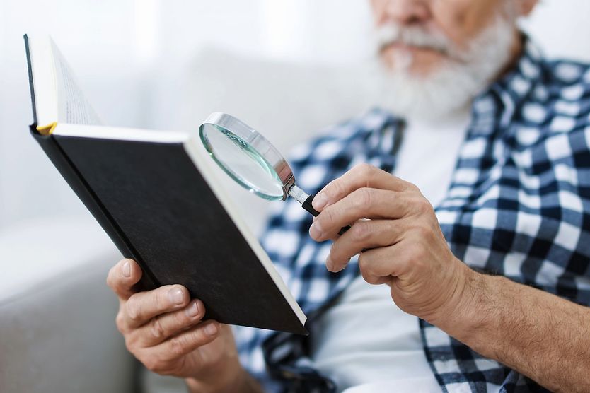 elderly man using low vision magnifier to read a book