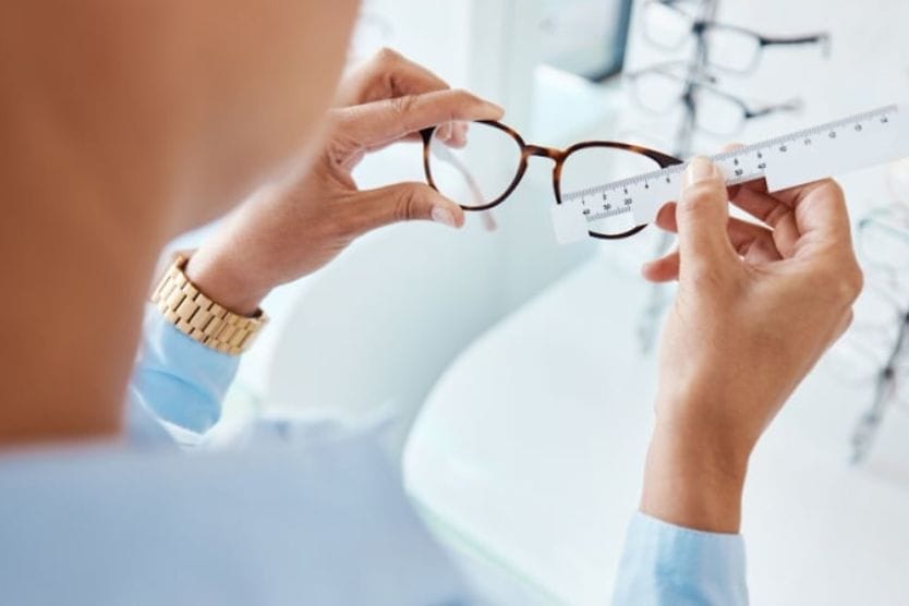 An optician measuring the frame size of a pair of glasses with a ruler at the eye doctor.