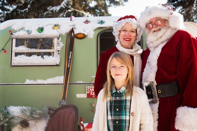 Santa and Mrs. Claus standing by a child wearing glasses