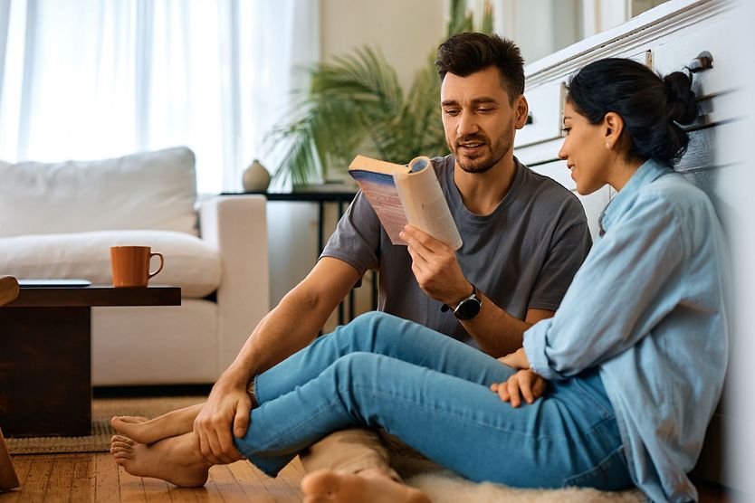 How long does lasik last. Smiling man reading book to his wife while spending time together at home.