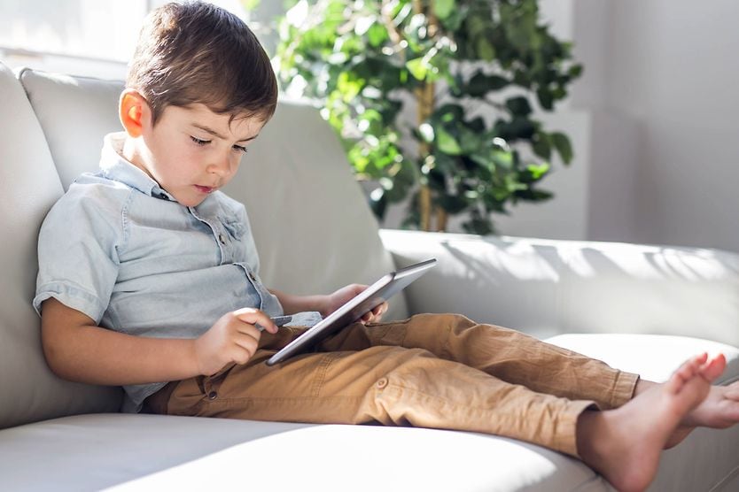 Un bambino usa un tablet sul divano, illustrando le abitudini legate all'uso degli schermi che causano affaticamento visivo digitale nei bambini