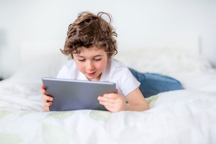 Un bambino che fissa lo schermo di un tablet mentre è a letto. Un bambino che fissa lo schermo di un tablet mentre è a letto.