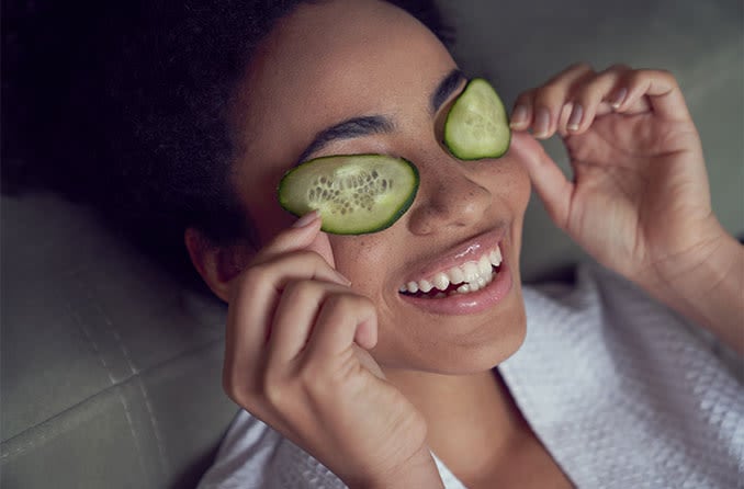 woman with droopy eyelids putting cucumber on her eyes as a home remedy