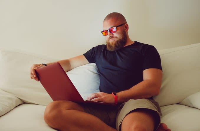 Bearded man wearing amber-tinted blue light blocking glasses while using a laptop