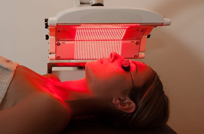 woman under a red light lamp (undergoing red light therapy)