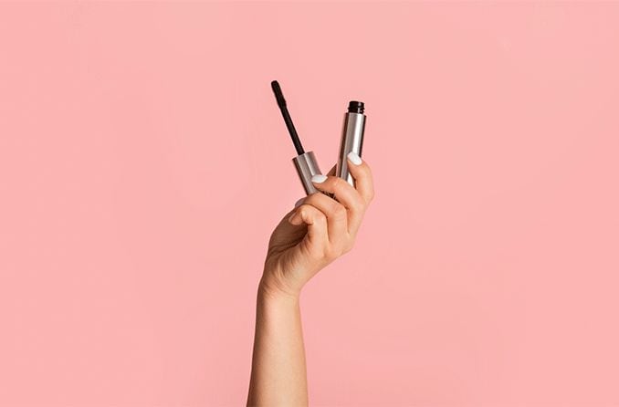 person's hand holding hypoallergenic mascara on pink background