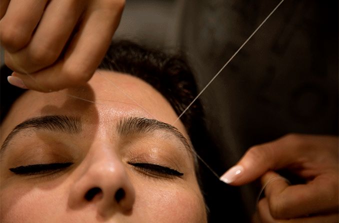 woman getting eyebrow threading procedure