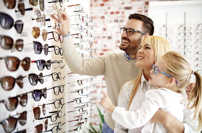 Happy family looking at eyeglass frames in an optical store - FSA