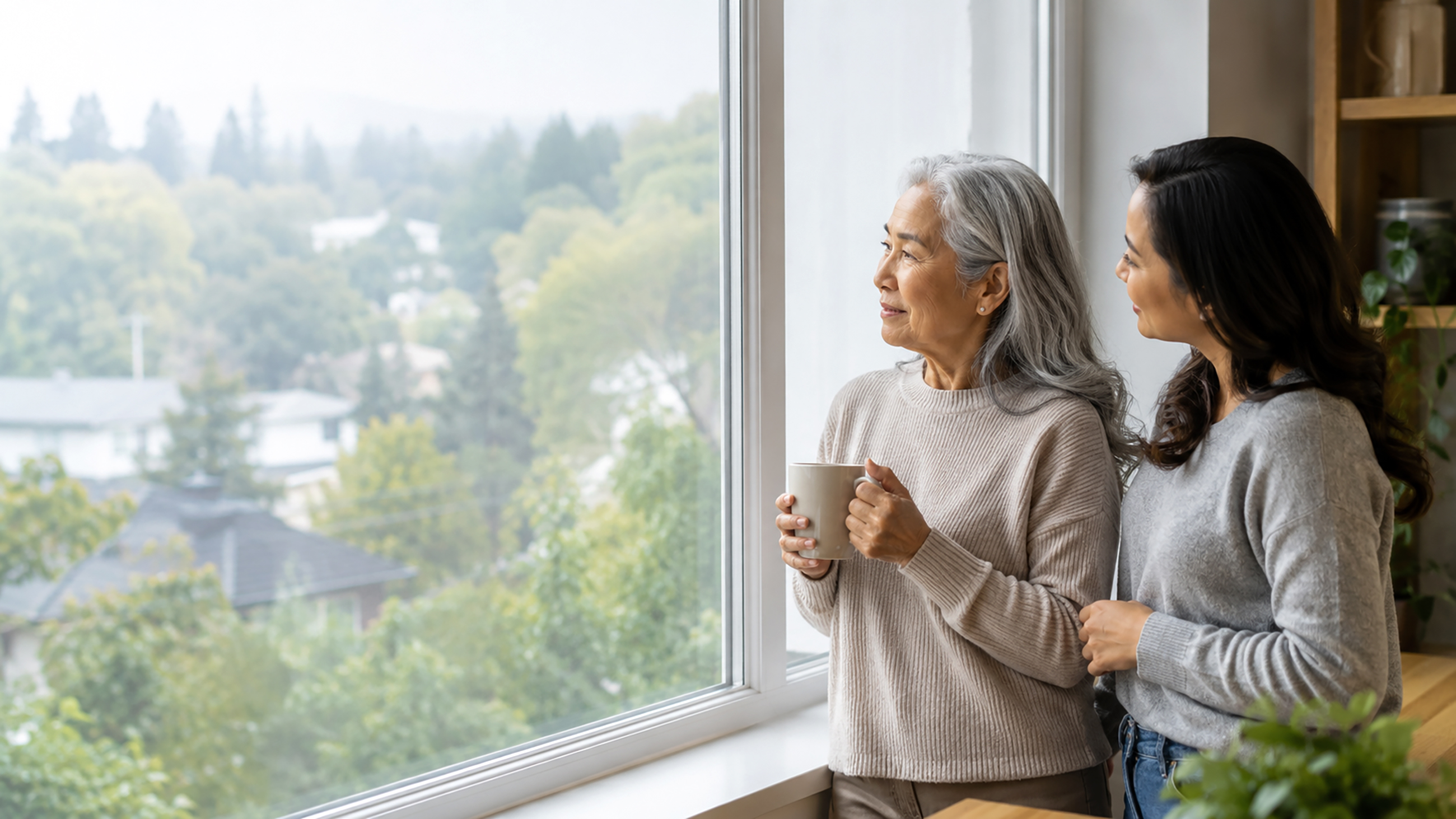Mother and daughter standing near a window, looking out at the trees.
