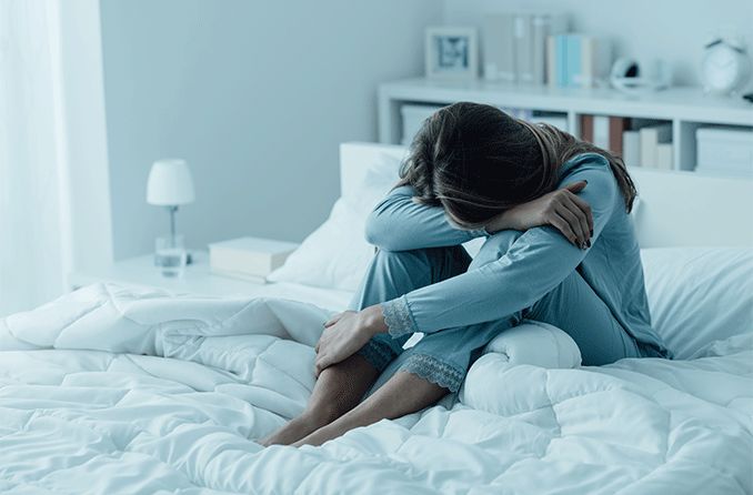 woman depressed in bed with her head in her lap