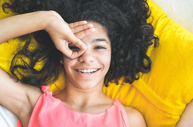 adolescent girl laying down looking through hole created through her fingers