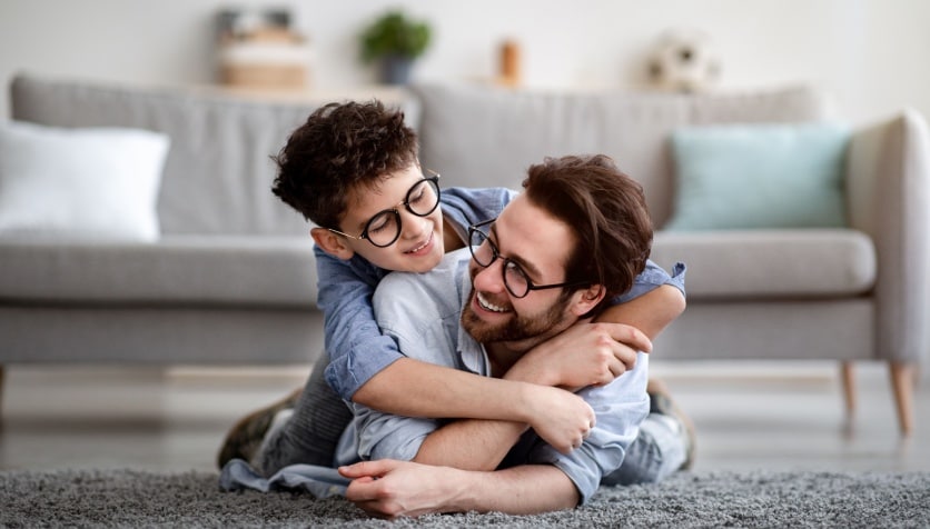 A father and son who are both wearing glasses for myopia hugging, showing how myopia may be genetic.