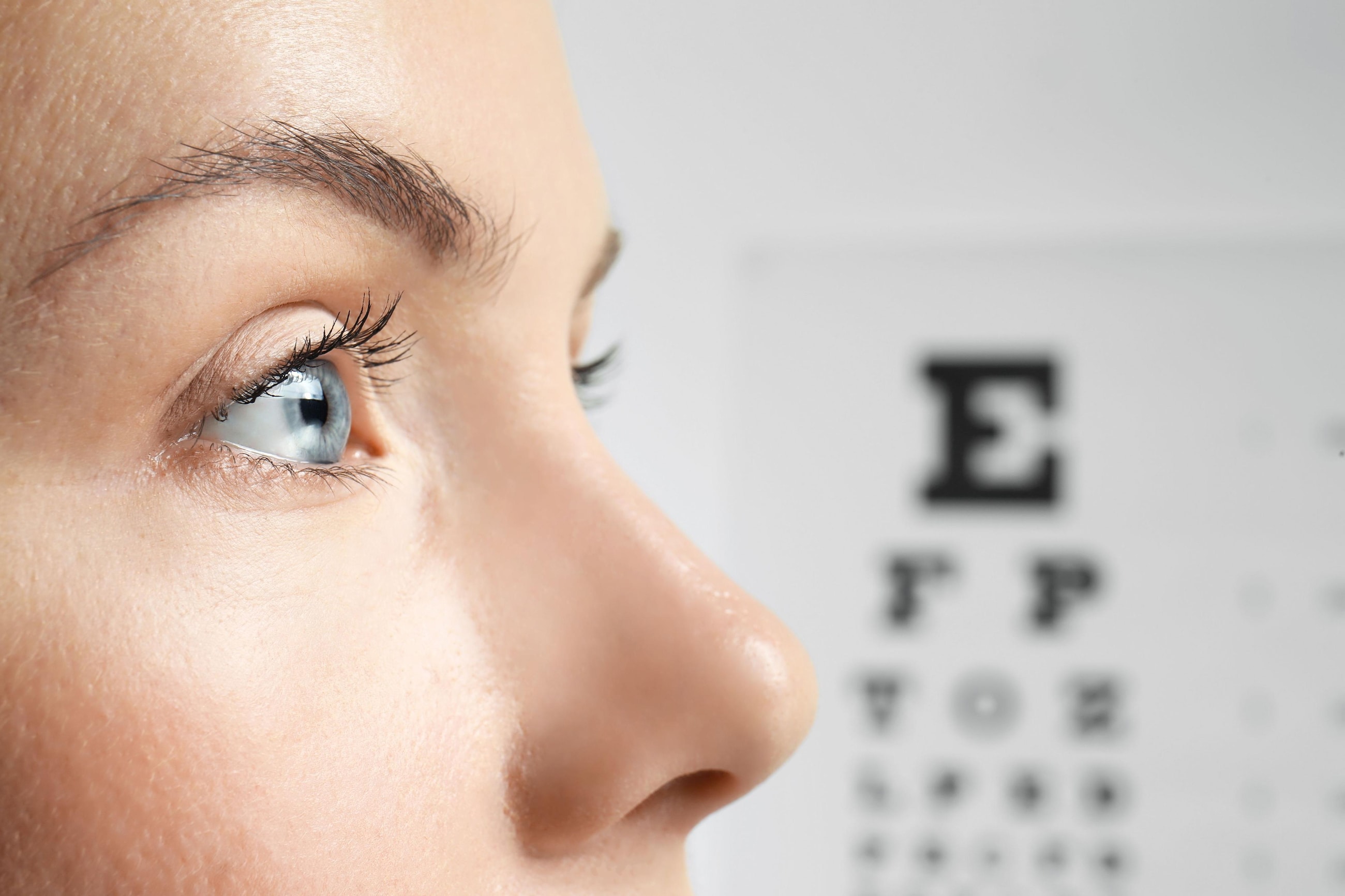 A profile image of a woman in front of a Snellen eye chart at a doctor's appointment for myopia.